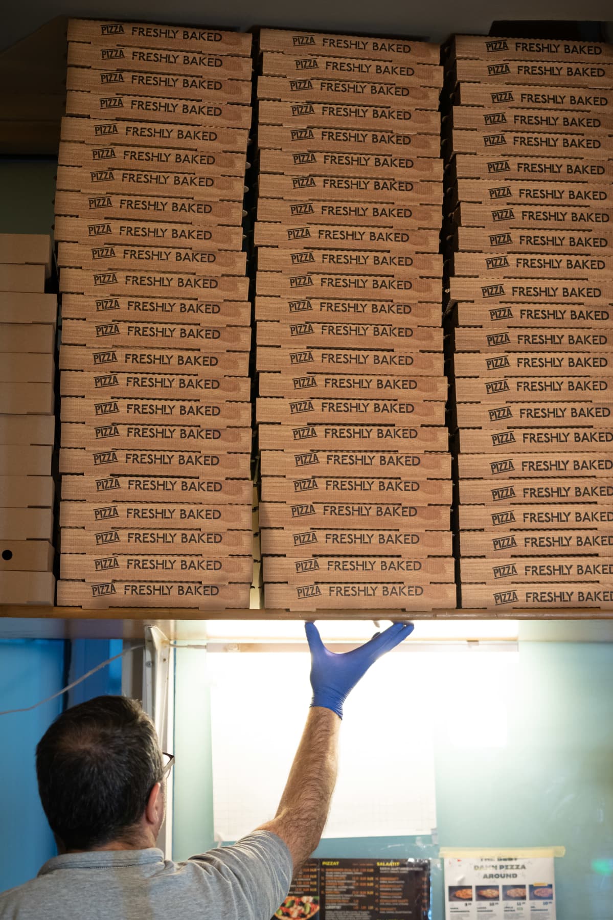 Beshir Peci ottaa pizzalaatikoita hyllyltä.