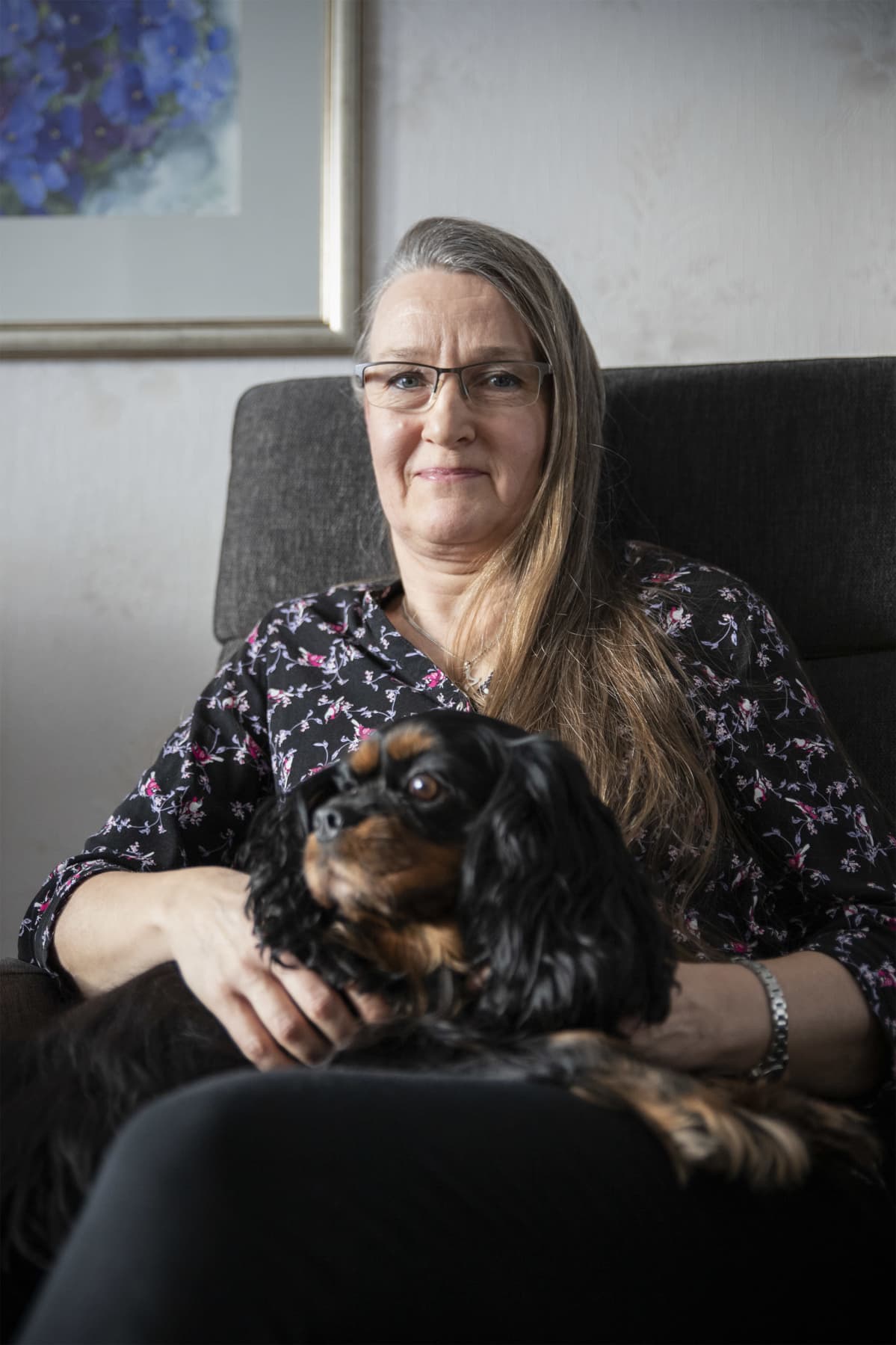 Tuula Porkka istuu nojatuolissa musta Heta-koira sylissään.