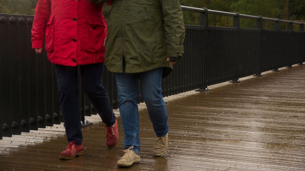 Kaksi naista kävelee sateessa sillalla.