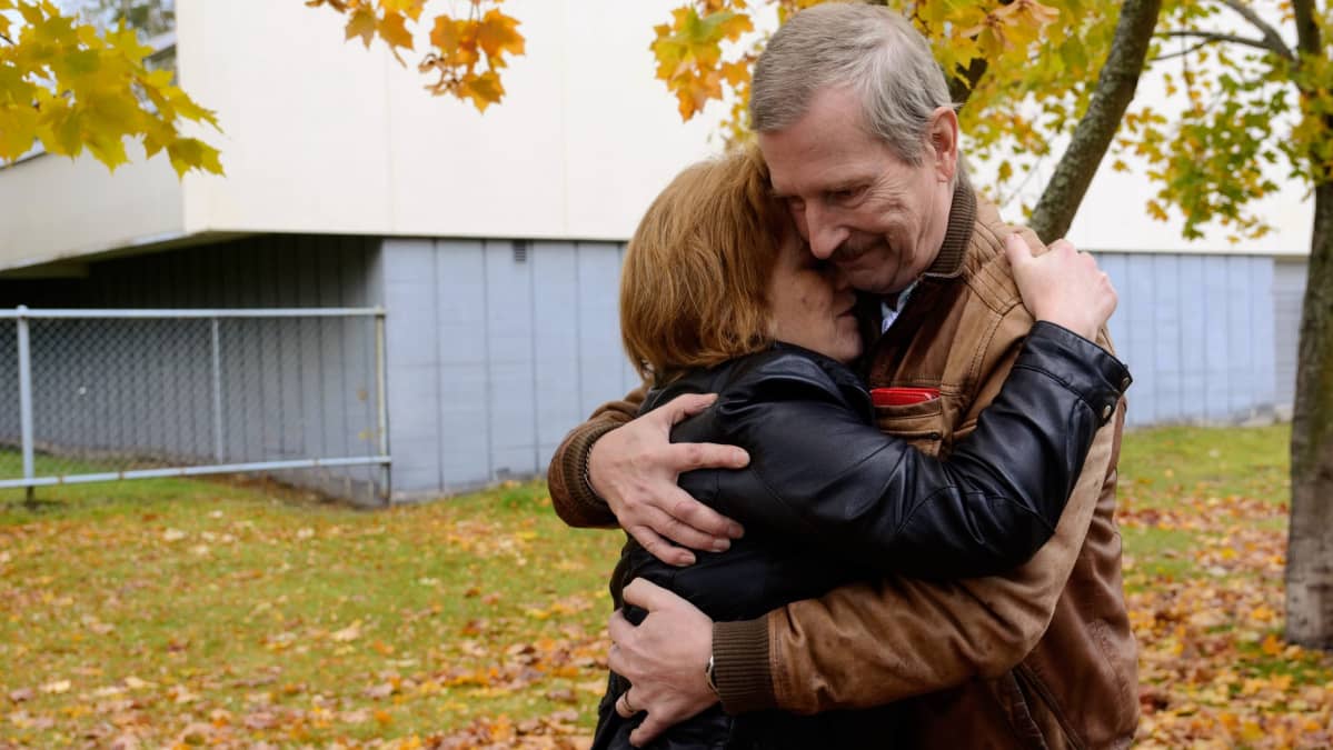 Nainen ja mies halaavat syksyisten puiden alla.
