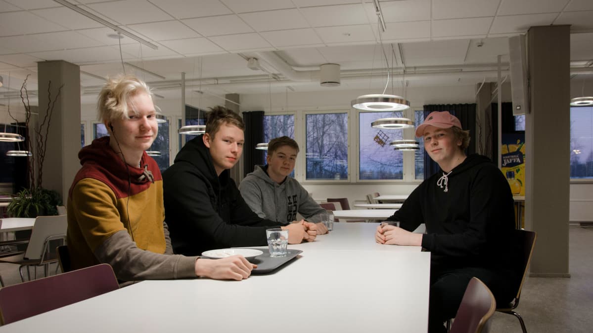 Opiskelijoita istuu pöydän ääressä koulun ruokalassa.