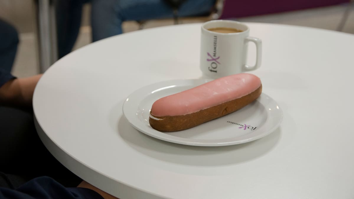 Berliininmunkki ja kahvikuppi koulun ruokalan pöydällä.