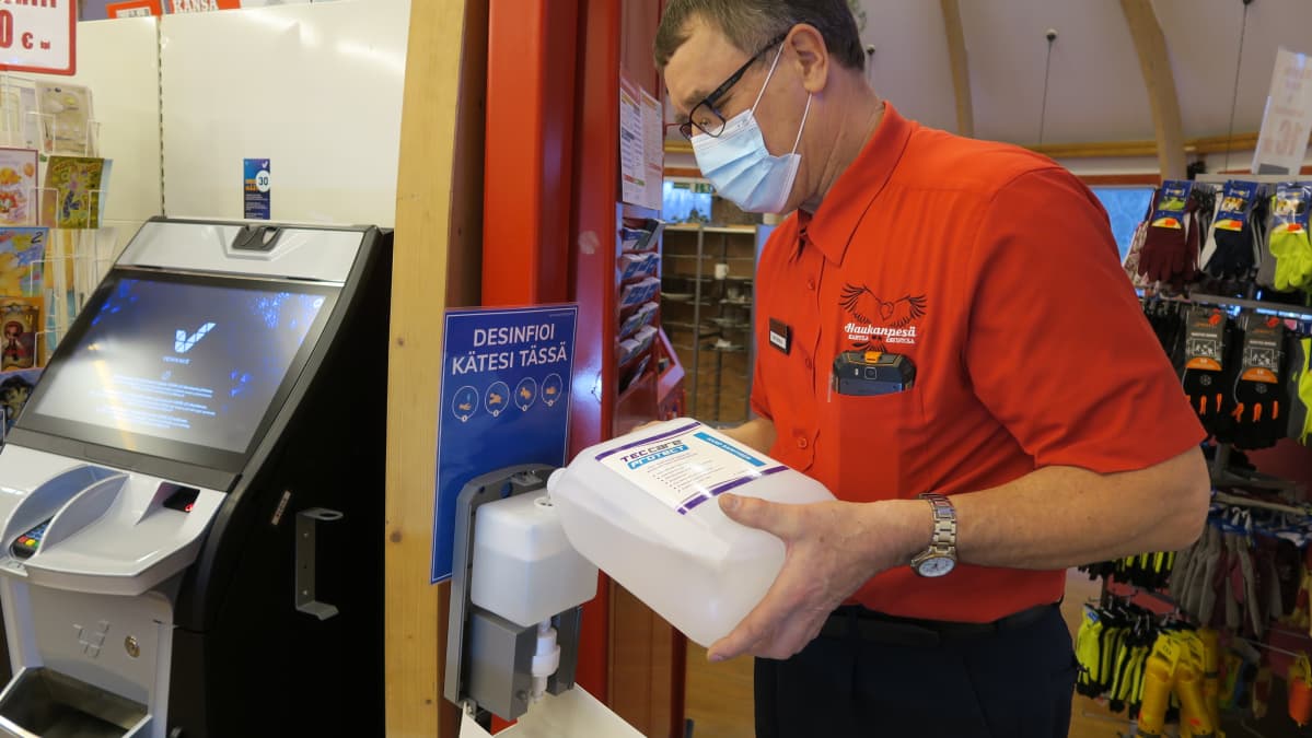 Ykköspesän yrittäjä Ahti Norja täyttää käsidesiautomaattia. - Asiakkaat kyllä käyttävät tätä todella innokkaasti, ei oikeastaan kukaan kävele ohi tullessa eikä lähtiessä, hän kiittää.