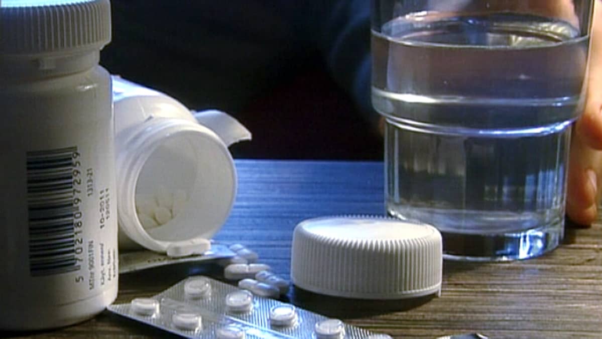 Henkilö tarttumassa vesilasiin ja pillereitä pöydällä.