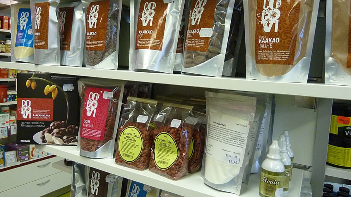 Superfoodeja luontaistuotekaupan hyllyllä, esimerkiksi kaakaopavut, kaakaovoi, goji-marjat ja maca-jauhe.