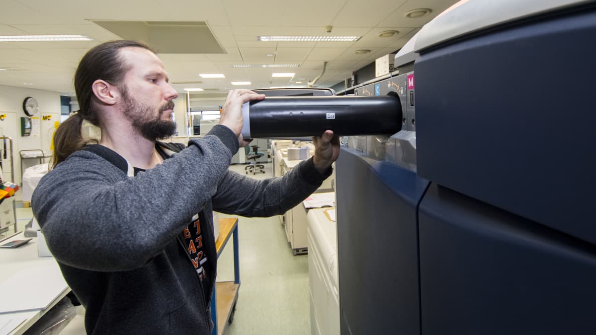 Painotalon työntekijä vaihtaa digitaalipainon värikasettia.