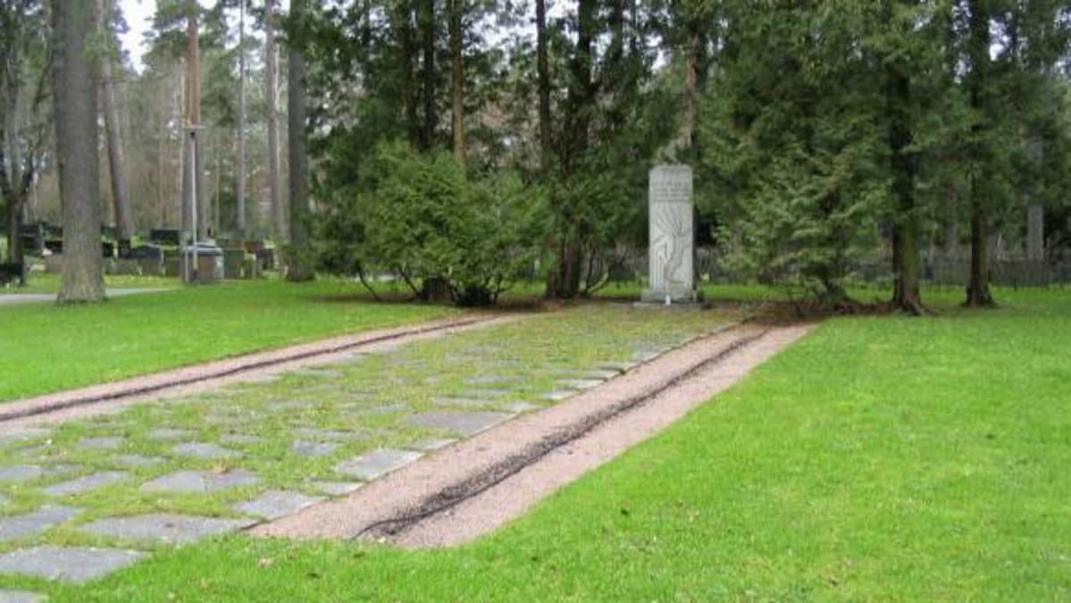 Muistomerkki hautausmaalla, puiden katveessa.