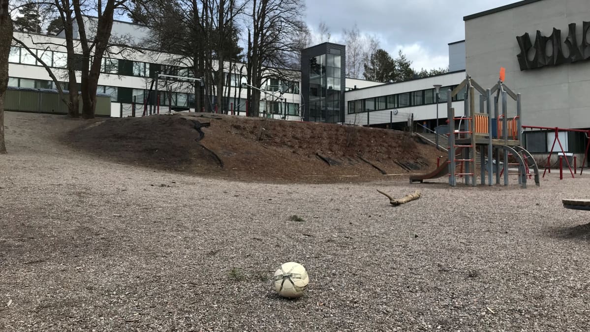 Koulun piha on tyhjä oppilaista. Pihalla on yksinäinen pallo.