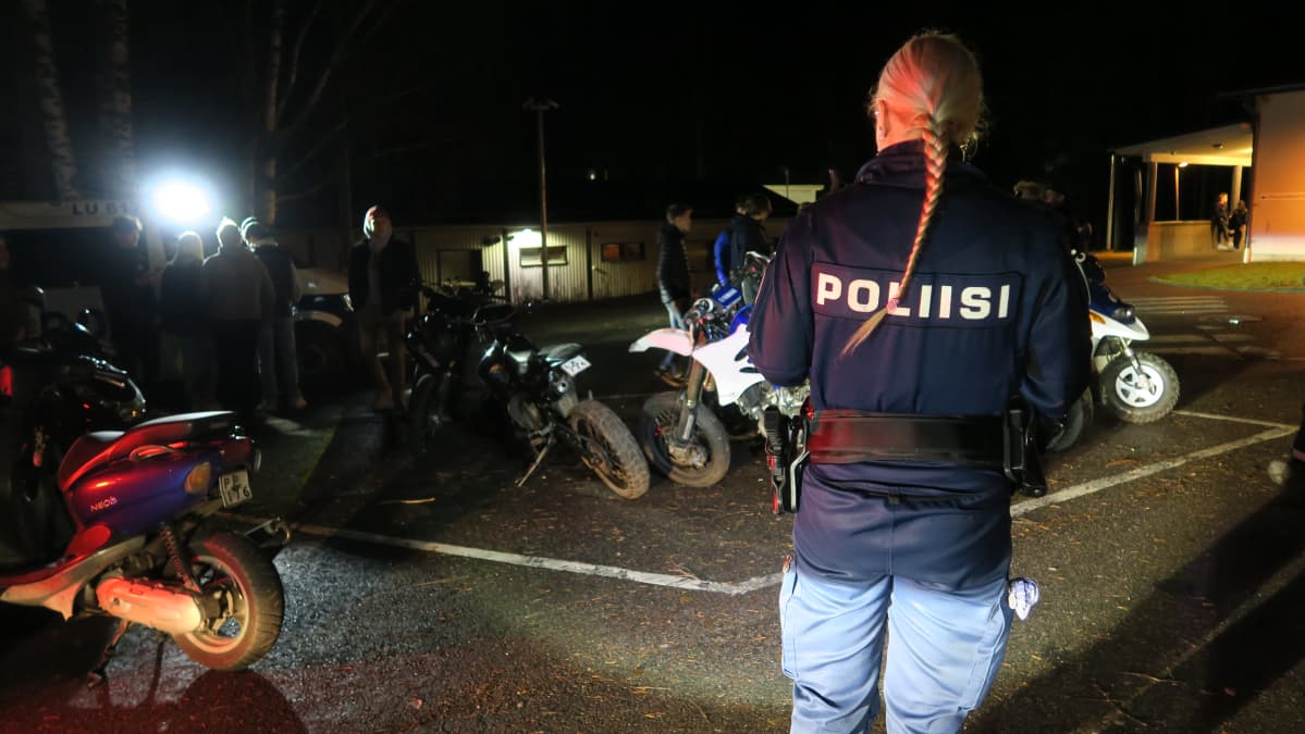 Poliisi tutkii mopoja koulun pihalla taskulampun valossa.