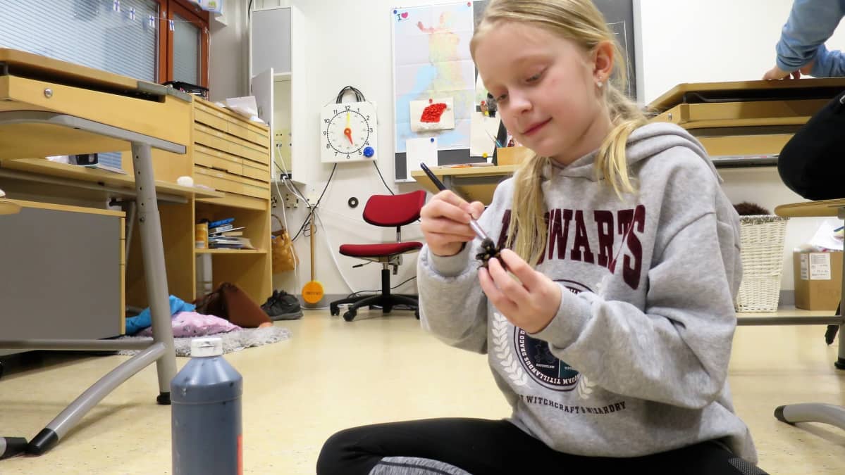 Nuori tyttö askartelee käpykranssia luokan lattialla