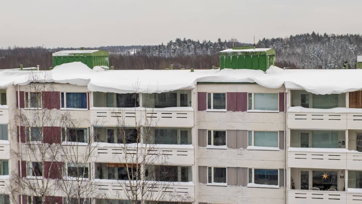 Kerrostalon katon reunalla näkyy valtavia lumikinoksia.