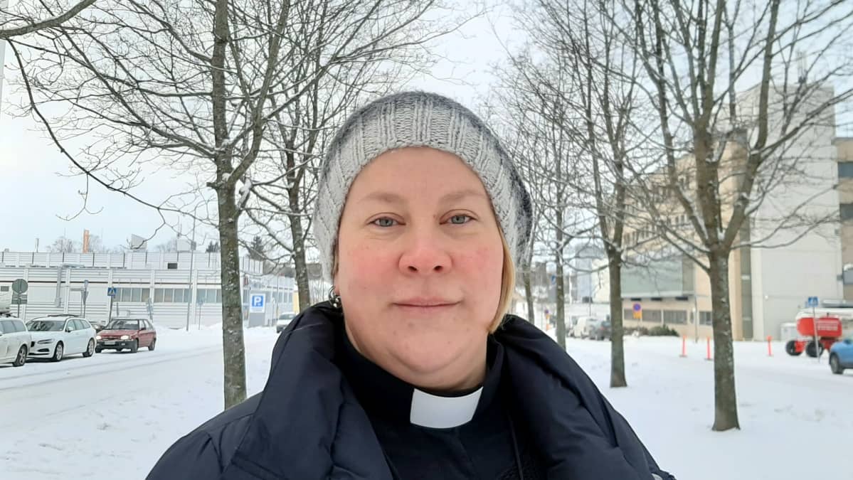 Nainen katsoo kameraan talvimaisemassa. Hänellä on kaulassa evankelisluterilaisen papin liperit.