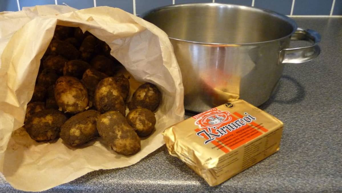 Multaisia perunoita paperipussissa tiskipöydällä, vieressä kattila ja voipaketti.
