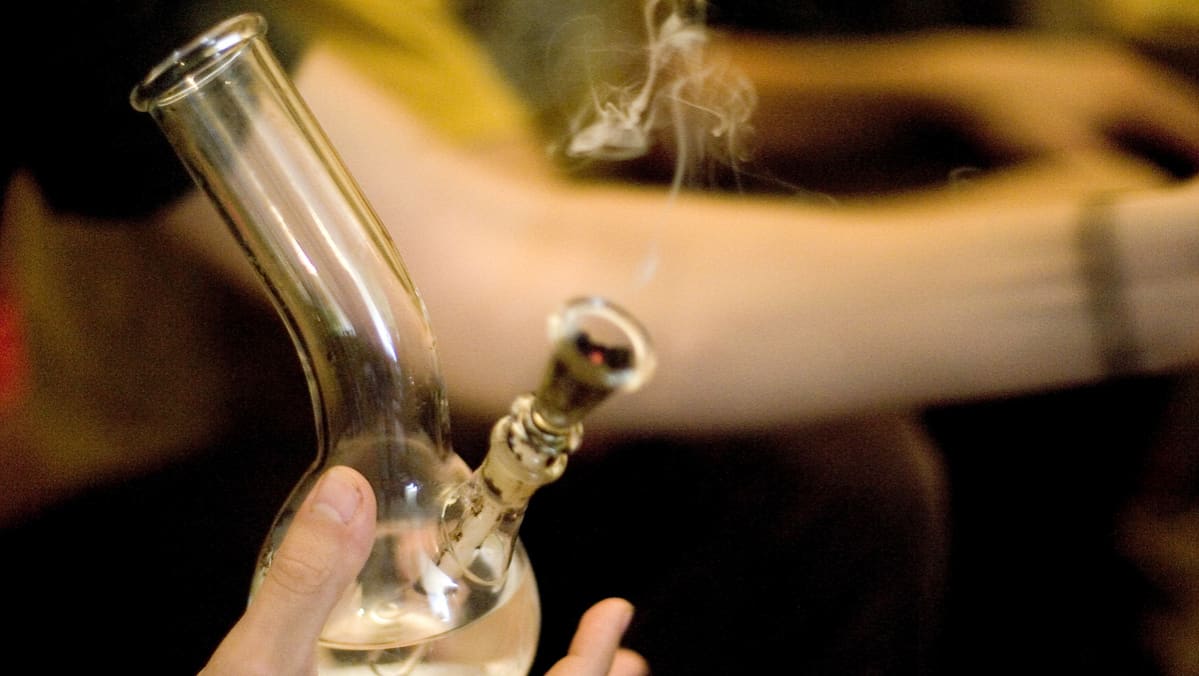 Lasinen kannabispiippu, jota pitelee naisen käsi.