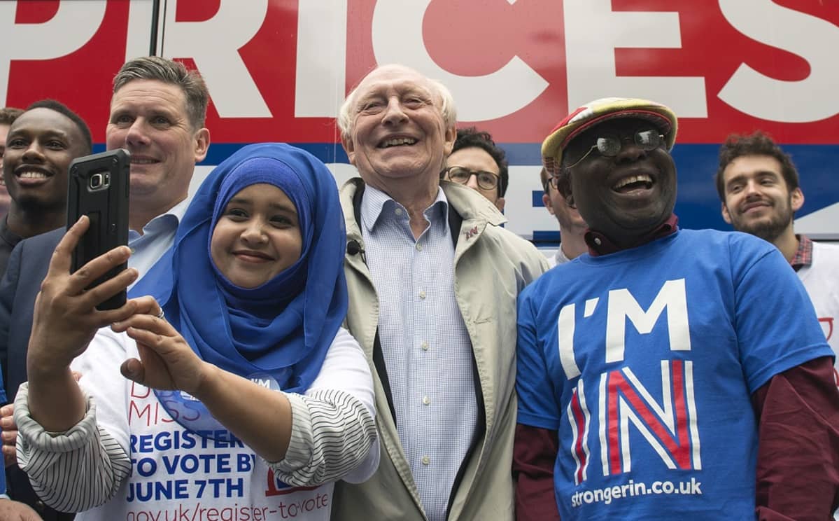 Kinnock hymyilee kannattajien keskellä. Nuori nainen ottaa selfietä.