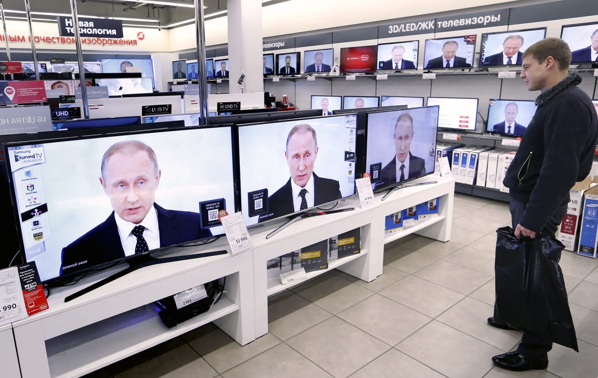 Venäläinen mies katsoo Putinin puhetta televisiosta elektroniikkakaupassa.