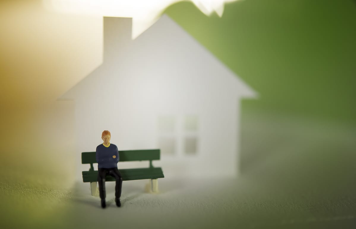 Miniatyyrimies istuu penkillä talon edessä.