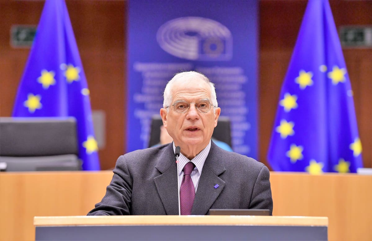 Josep Borrell puhuu puhujanpöydän takana salissa. Hänellä on harmaa puku ja violetti kravatti. Takana ylemmällä korokkeella näkyy kaksi EU:n lippua.
