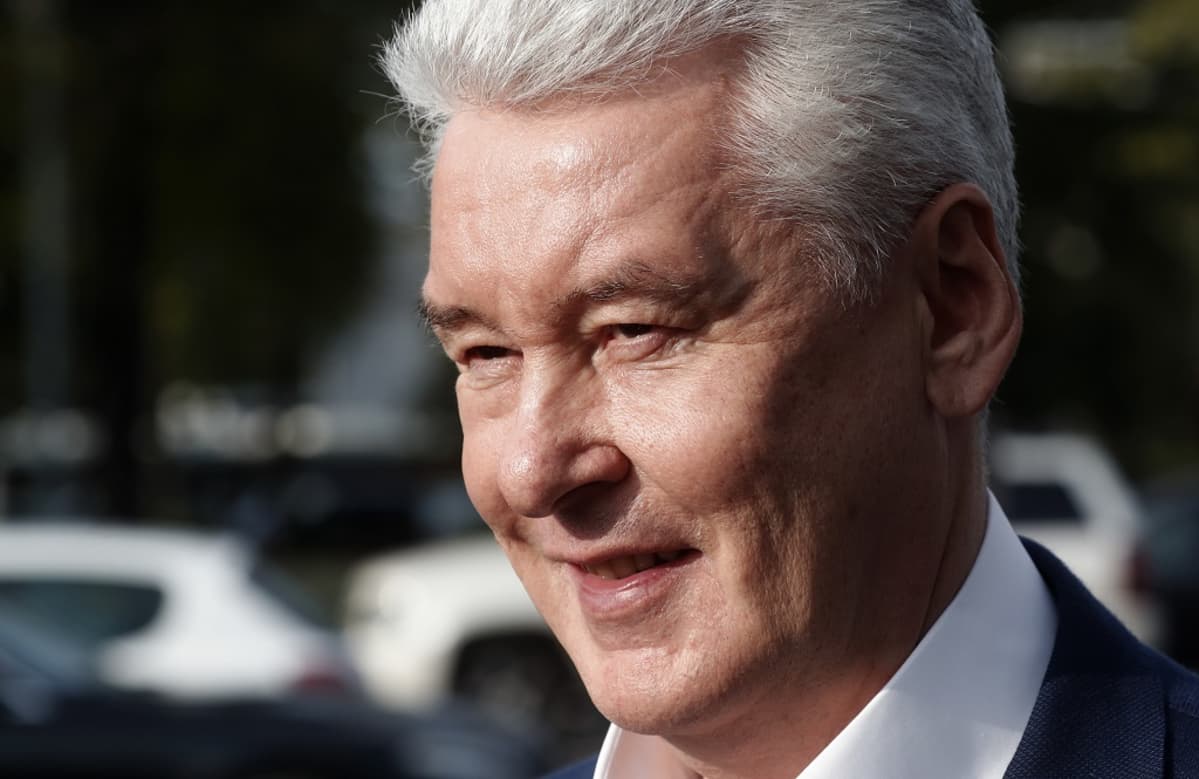 Harmaahiuksinen Sobjanin hymyilee kuvattuna tummaa taustaa vasten.