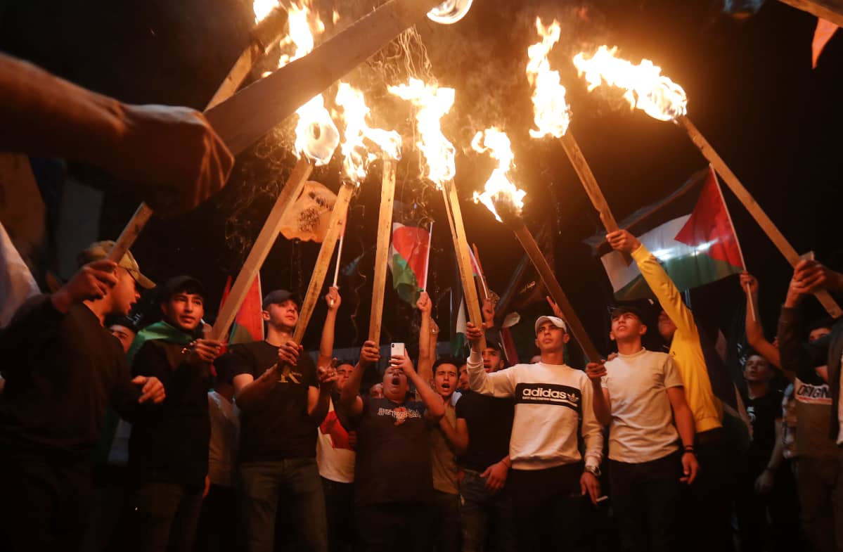Palestiinalaiset osoittavat mieltään lippujen ja soihtujen kanssa.