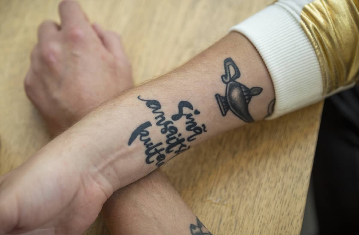 Homopojan oppaan kirjoittajan Eino Nurmiston kädet, joissa tatuointi, jossa lukee "Sinä ansaitset kultaa".