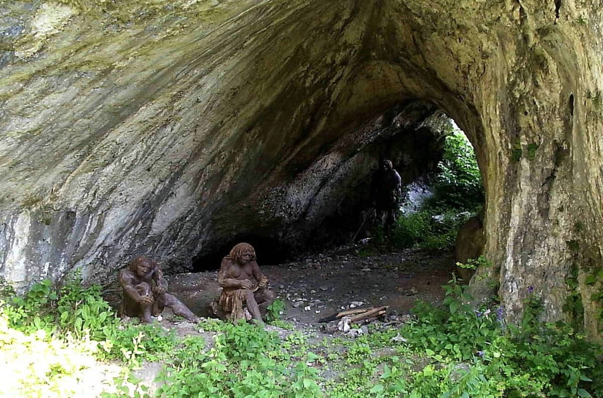 Kaksi neandertalilaisia esittävää nukkea luolan suulla.