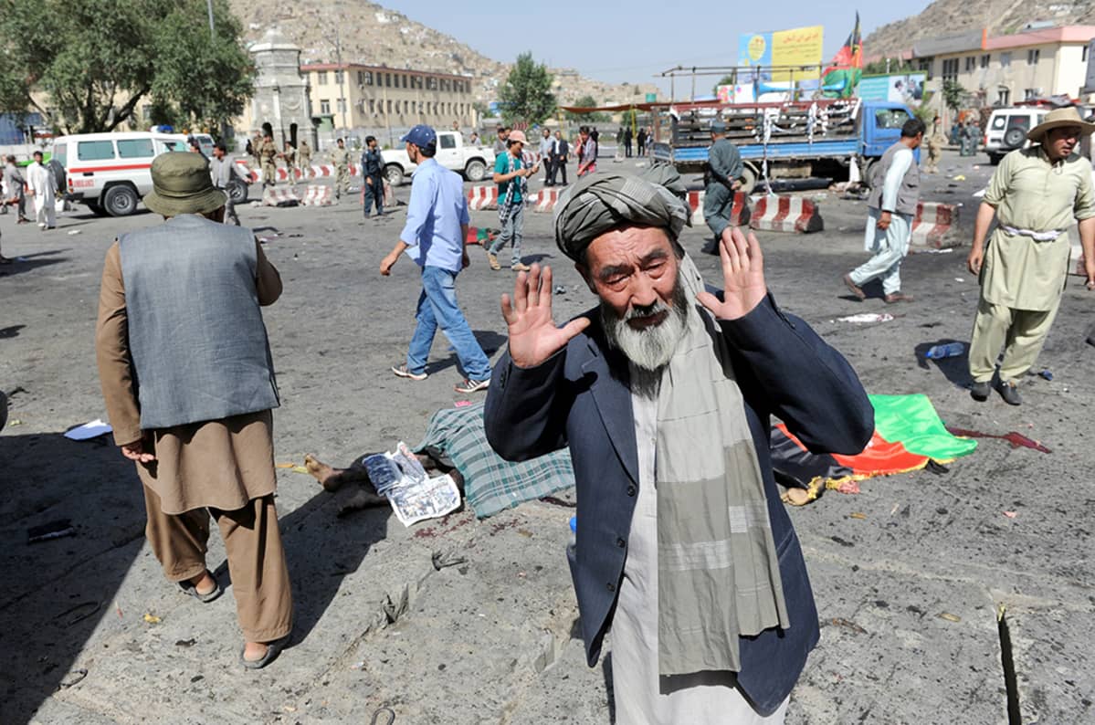 Etualalalla mies, jonka takana kaksi peitettyä ruumista