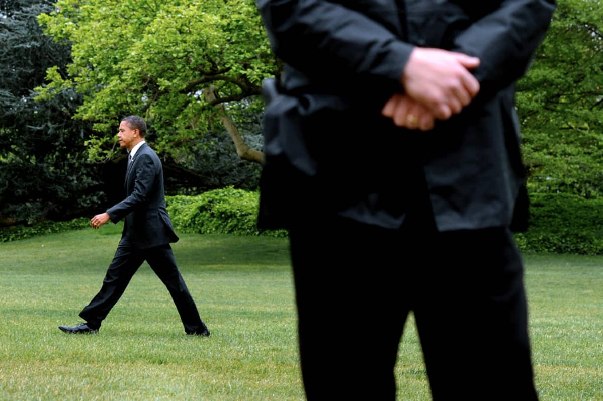 Yhdysvaltain presidentti Barack Obama kävelee Valkoisen talon nurmikolla Salaisen palvelun miehen tarkkaillessa ympäristöä.