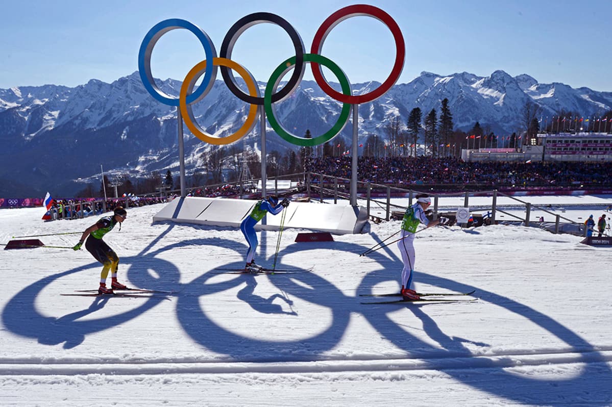 Naiset hiihtävät olympiarenkaiden ohi.