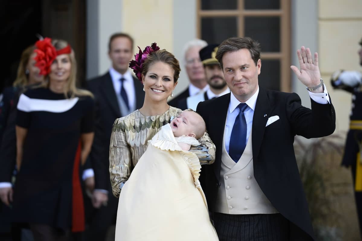 Madeleine lapsi sylissään, Chris vilkuutta vieressä.