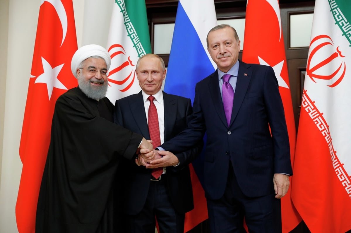 Hasan Rouhani, Vladimir Putin ja Recep Tayyip Erdoğan pitävät käsiään yhdessä ja poseeraavat kameralle maidensa lippujen edessä. 