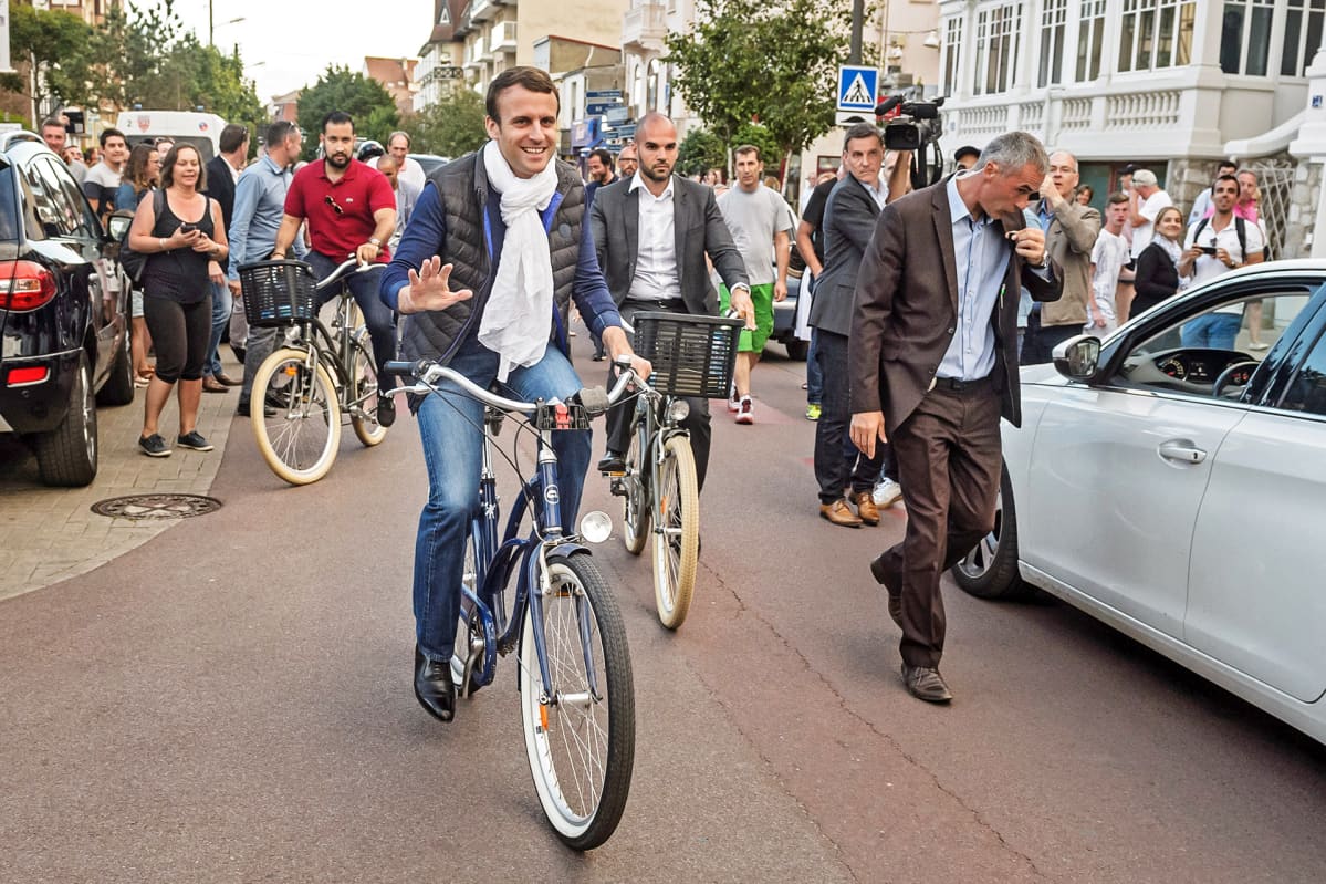 Emmanuel Macron pyöräilee kadulla.