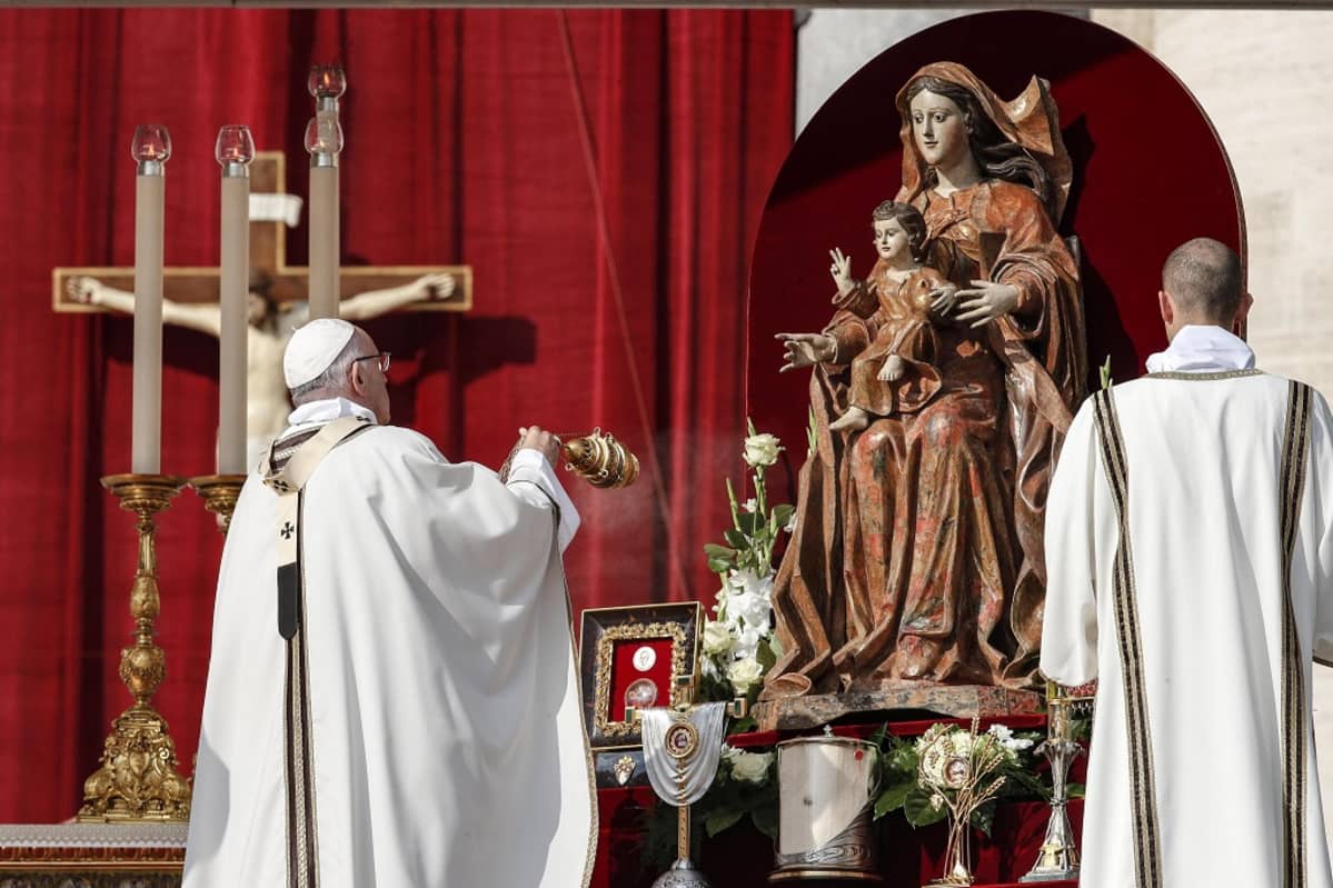 Paavi heiluttaa suitsukeastiaa Neitsyt Mariaa ja Jeesus-lasta esittävän patsaan edessä. Taustalla on punainen seinäkangas, jonka edessä on krusifiksi.