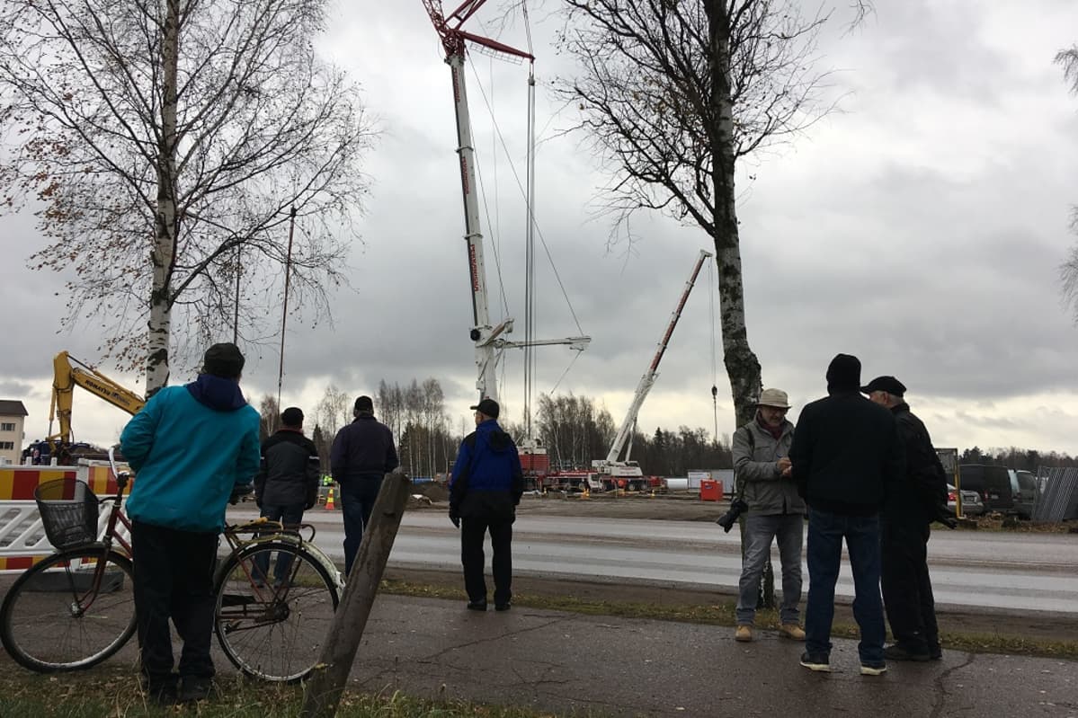 Ihmisiä katsomassa tien varressa satametrisen lipputangon nostoa pystyyn Haminassa.