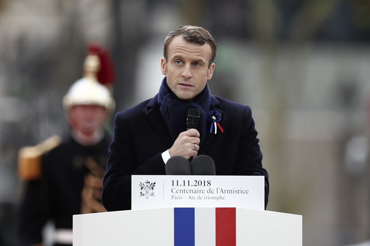 Emmanuel Macron puhujanpöntön takana. Hänellä on kädessään mikrofoni. Puhujanpöntössä on Ranskan lippu.