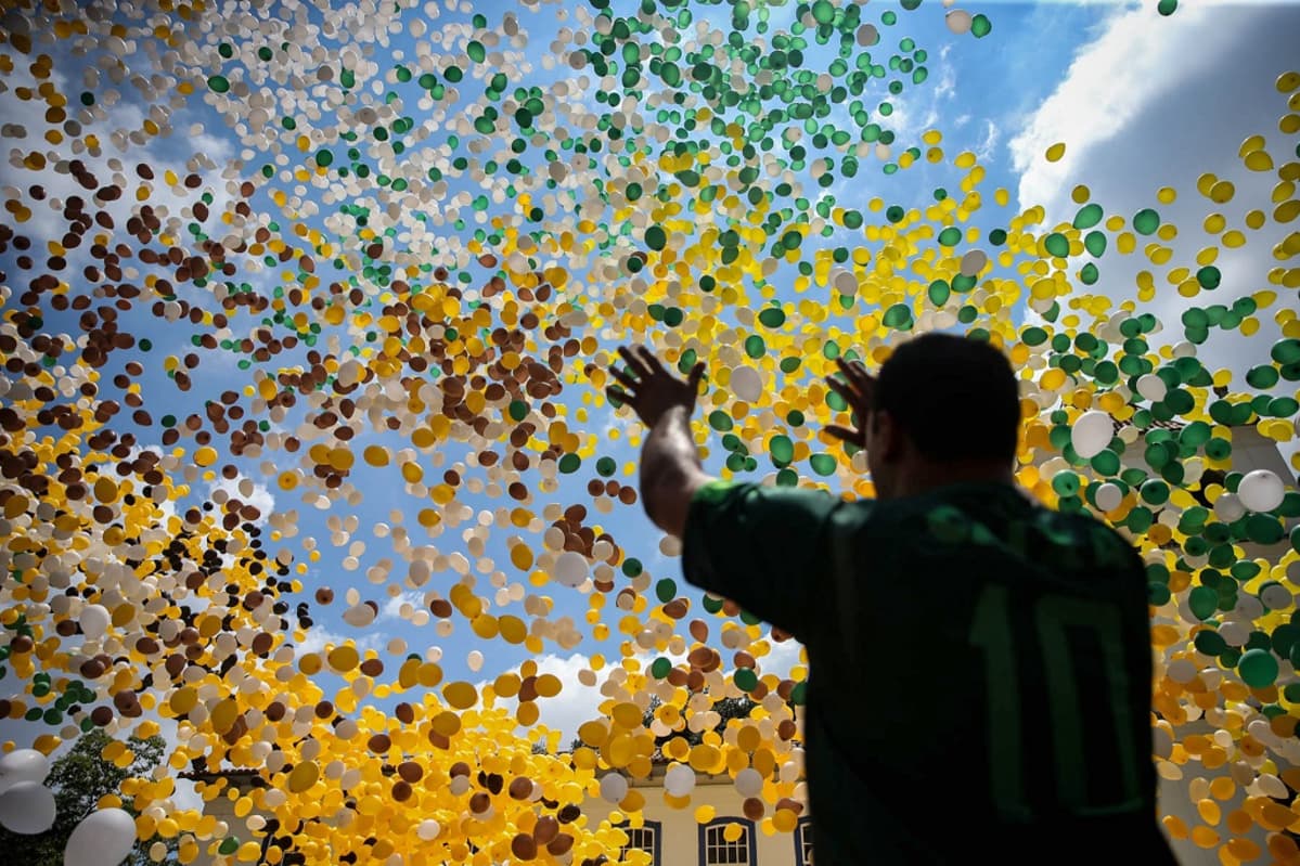 Mies ojentaa käsiään kohti taivaalle kohoavaa Brasilian lipun väristen ilmapallojen suurta parvea.