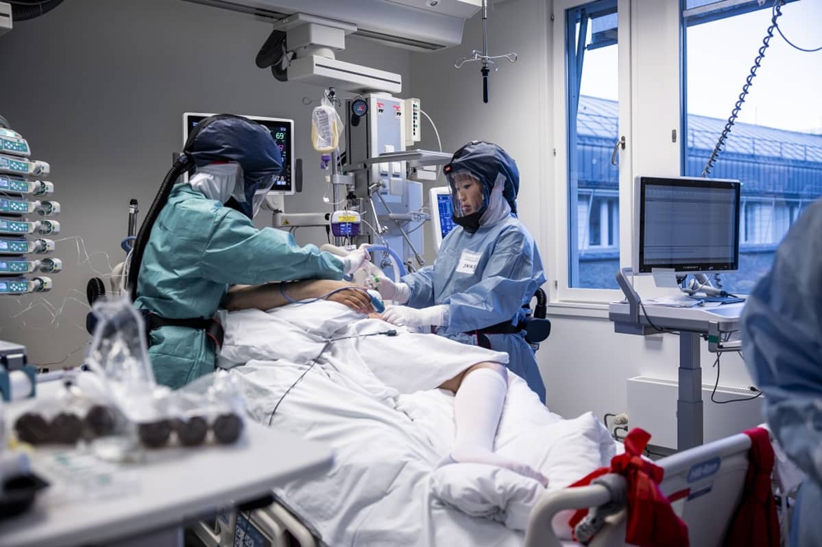 Suojavarusteiset työntekijät potilasvuoteen molemmin puolin.