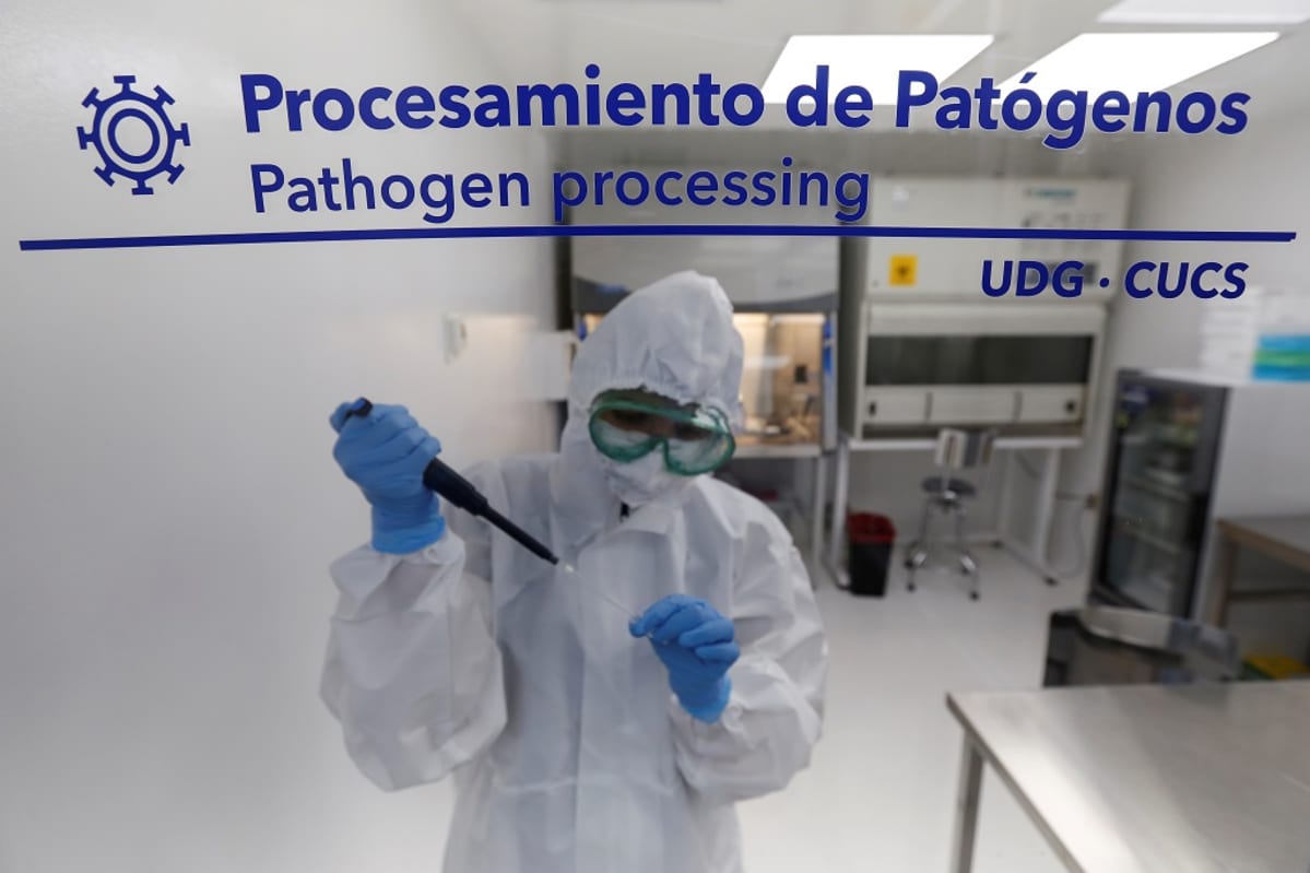 Laboratorion ikkunan läpi otettu kuva suojapukuisesta tutkijasta.