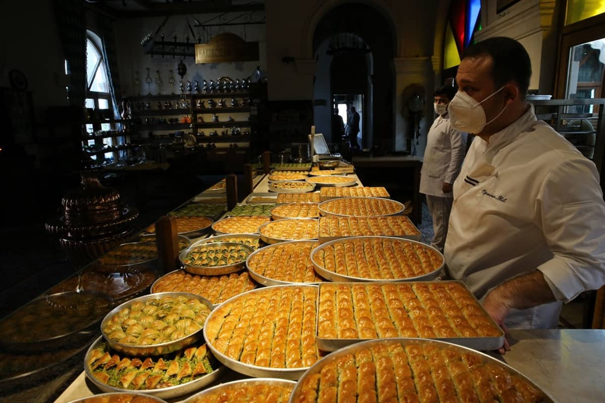 Kuvassa myyntipöydällä on Baklava-leivonnaisia. Pöydän takana seisoo kaksi miestä, jotka ovat leipomon työntekijöitä.