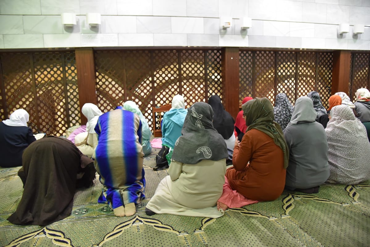 Hunnutetut naiset istuvat selin mattoon verhotulla lattialla edessään tähtikuvioinen säleikkö