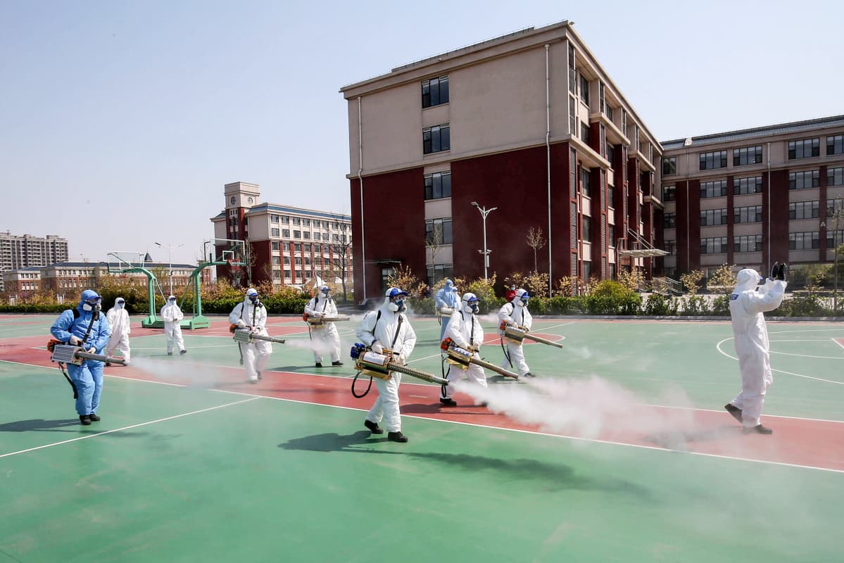 Suojapukuihin pukeutuneet vapaaehtoistyöntekijät desinfioivat koulun pihaa Kiinan Weifangissa.