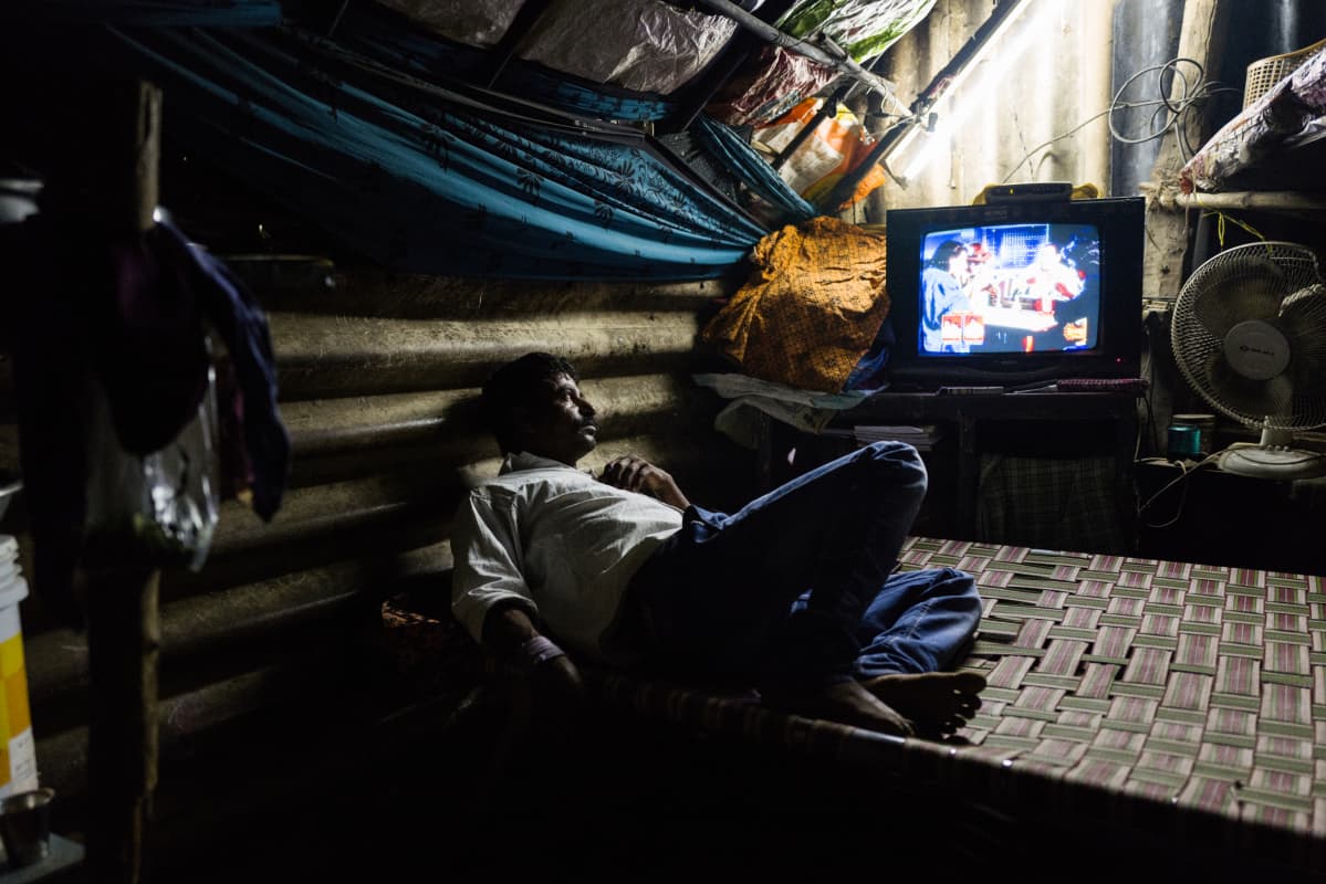 Mies makaa sängyllä ja katsoo televisiota.