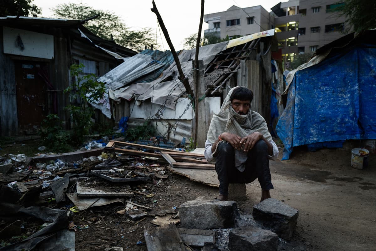 Mies istuu kivellä hökkeleiden ympäröimällä aukiolla slummissa.