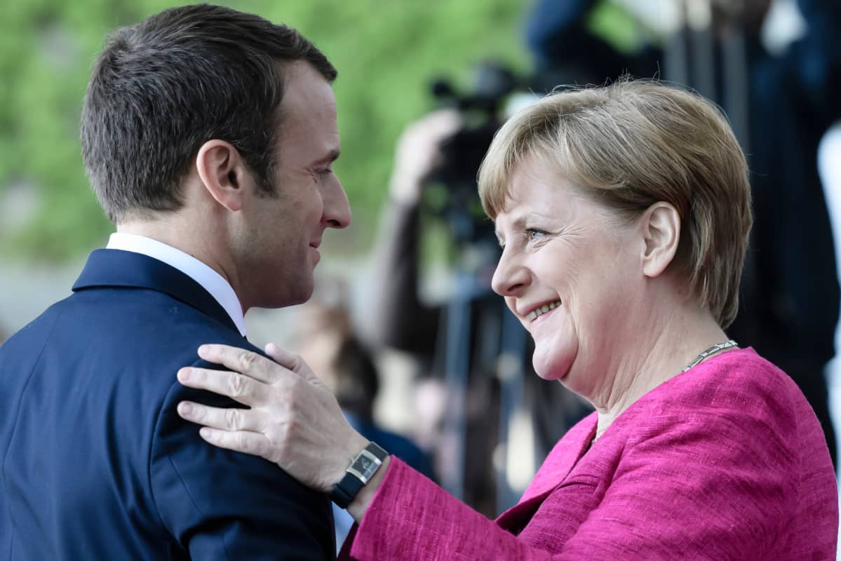 Macron ja Merkel tervehtivät.
