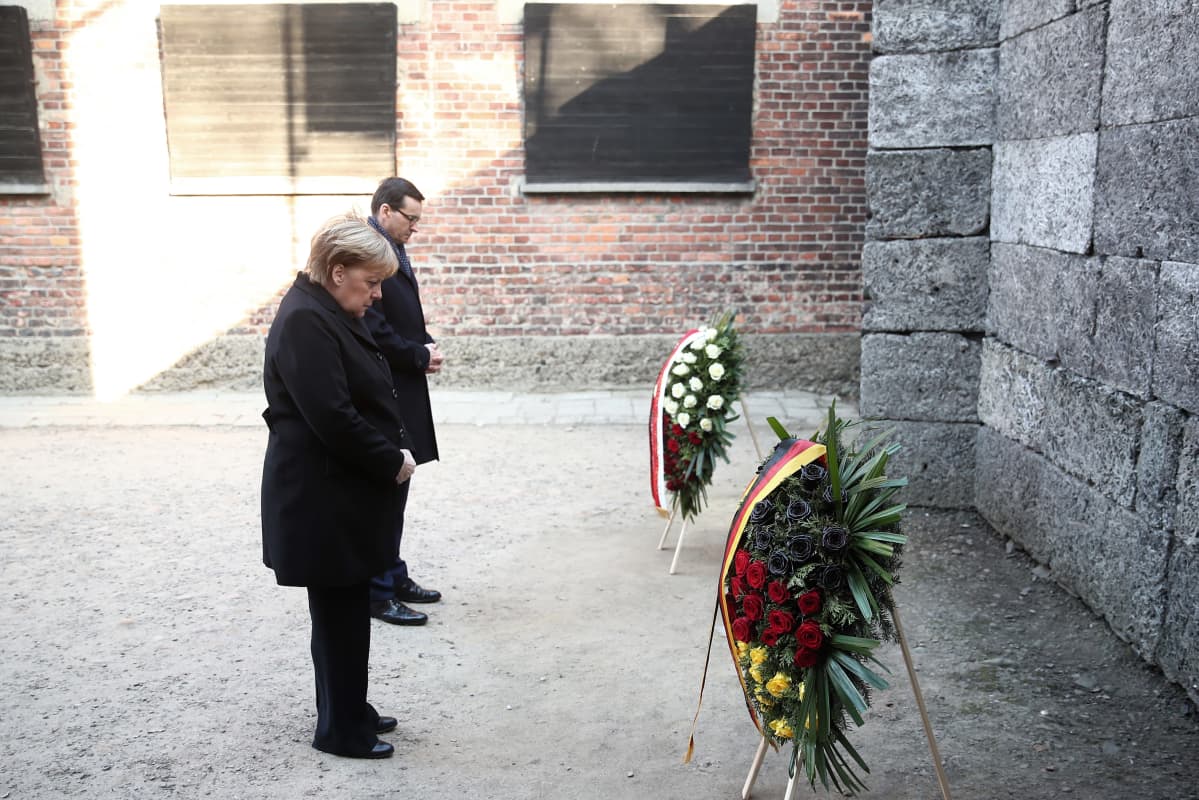 Angela Merkel ja Mateusz Morawiecki päät kumarassa kukkaseppeleiden edessä.
