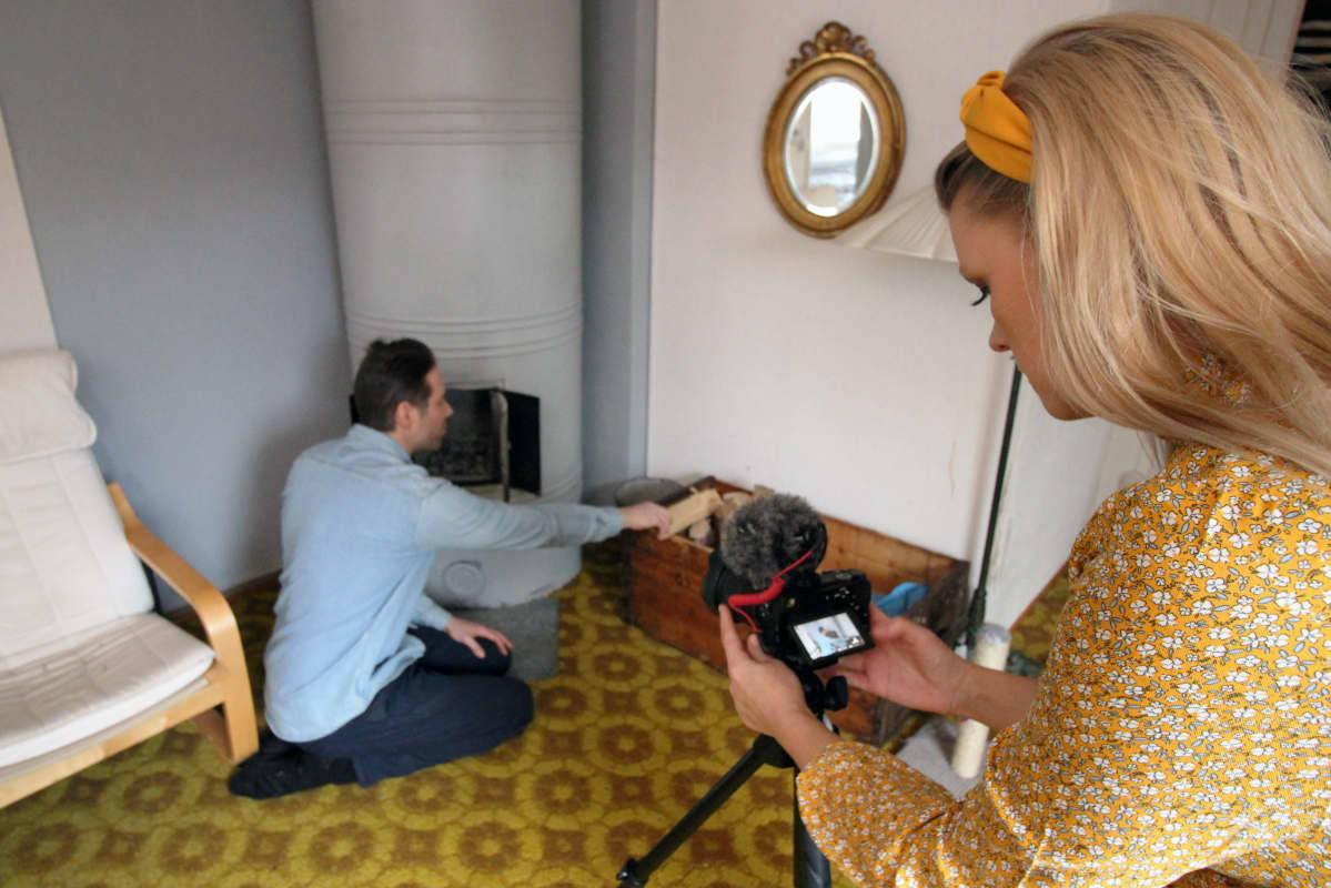 Anniina Jalkanen kuvaa kun Juha Jalkanen laittaa puita takkaan.