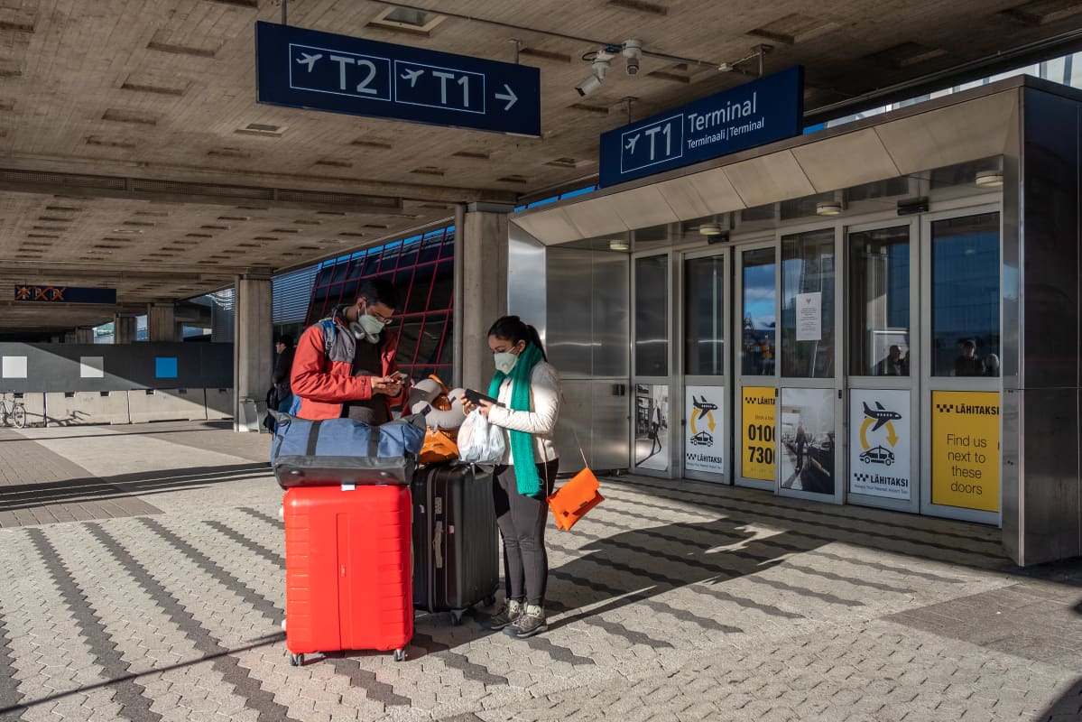 Helsinki-Vantaan lentoasemalla, Terminaali 1 edustalla, kaksi matkustajaa kasvosuojukset päällä.