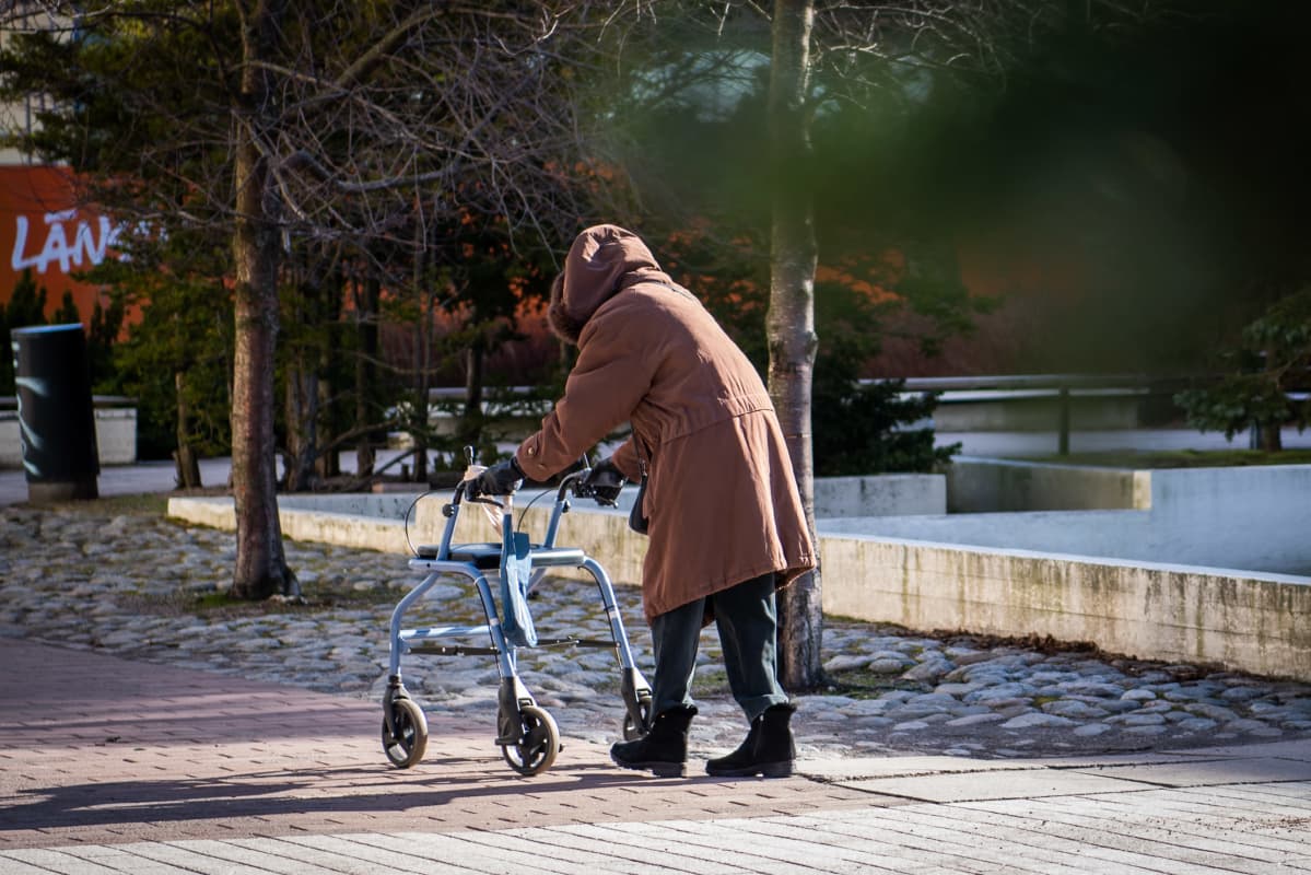 Vanhus rollaattorin kanssa kävelemässä kohti kauppaa.