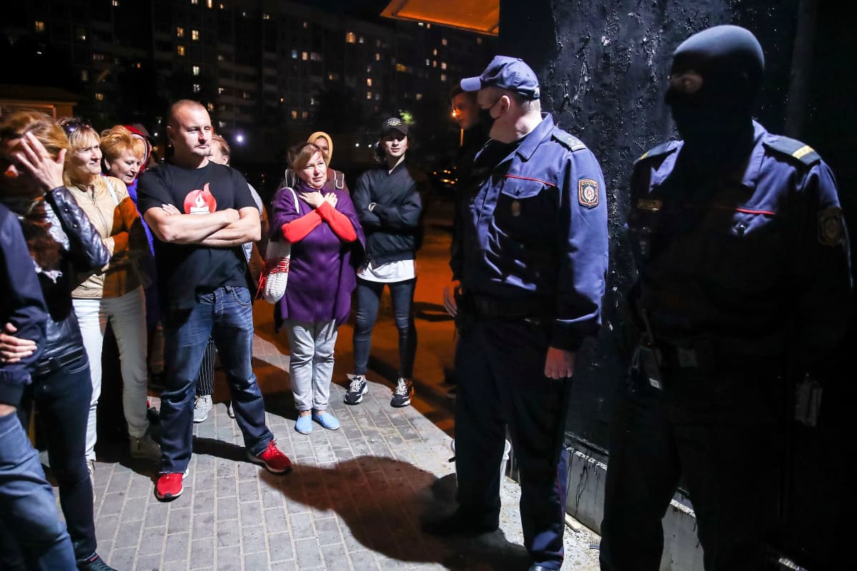 Kaksi poliisi vartioi mustaksi maalattua seinää. Protestoijat katsovat poliiseja uhmakkaasti. Toisella on päässään musta hiihtomaski, toisella kasvosuojain.