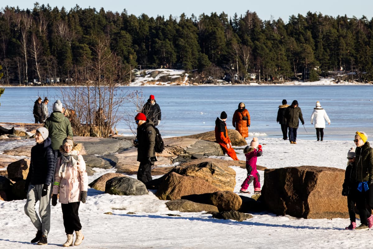 Ihmisiä ulkoilemassa meren rannalla.